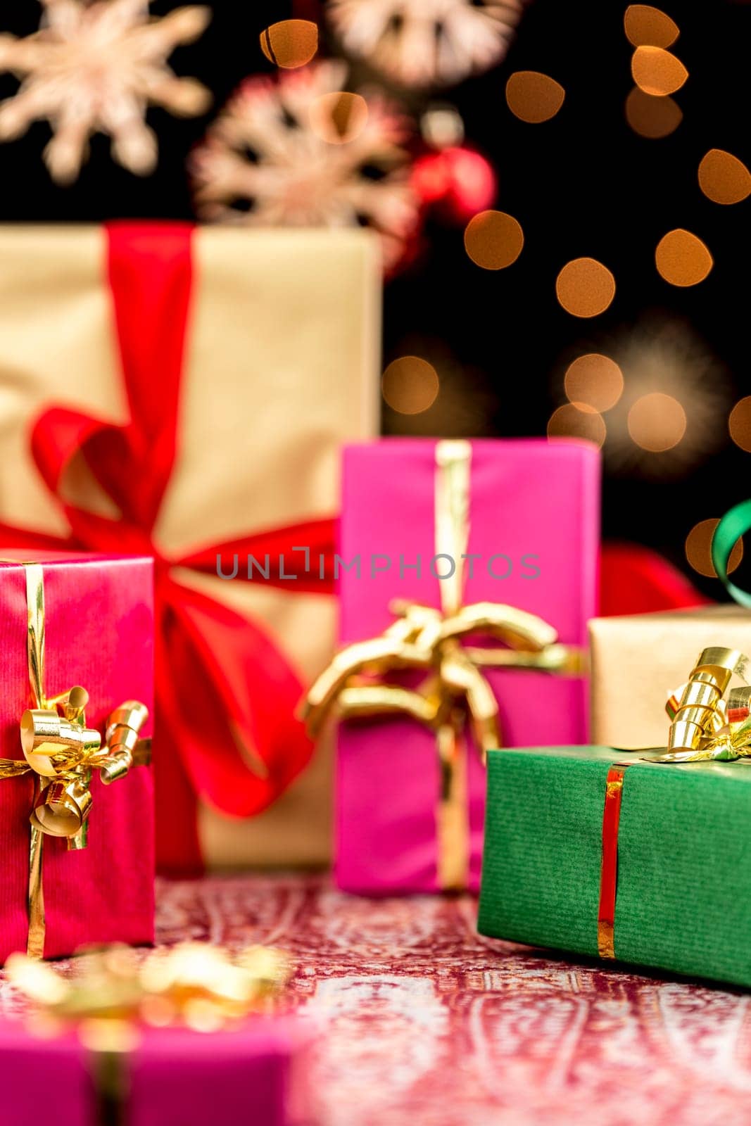 Tightly framed Christmas presents in red,green,magenta and golden colors. Sparkling orange light reflexes and blurry stars against pitch black.