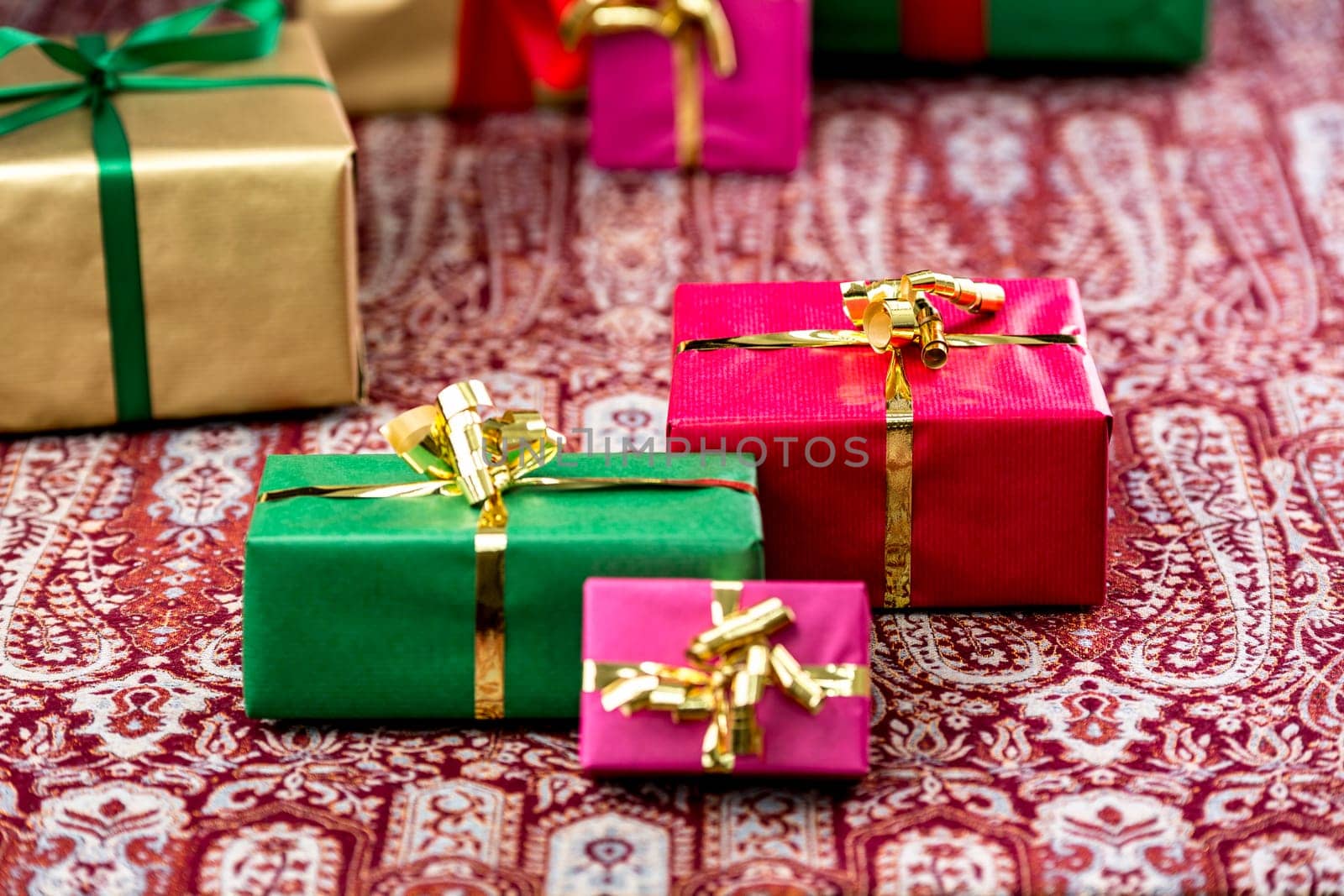 Single-colored gifts in magenta, green, red and gold placed on a festive cloth. Plenty of text space. Background for many gift-giving occasions.
