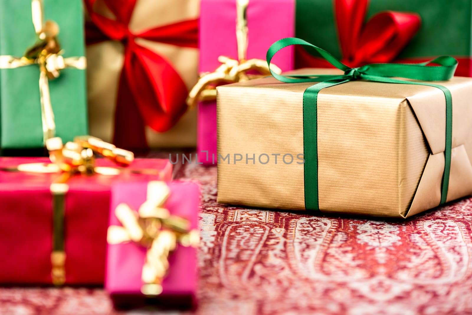 Golden gift box with emerald bow amidst other presents in magenta, red, green and gold. Tightly-framed shot with shallow depth of field. Fit for any gift exchange.