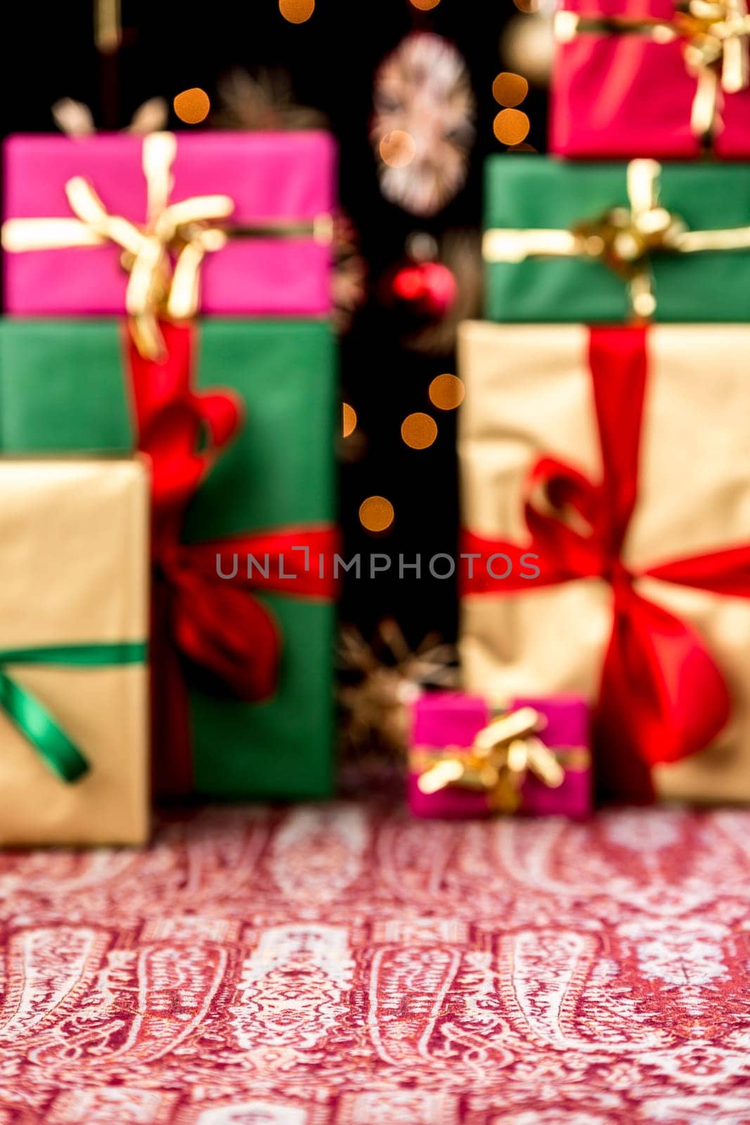 Christmas presents piled-up on a festive cloth. Wrapping and ribbons in gold, red, magenta and green. Twinkles and blurred stars in the back. Plenty of text space in void foreground.