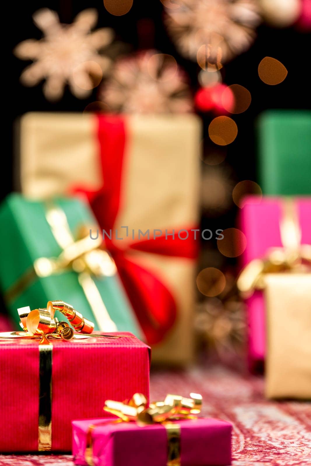 Twinkles,blurred stars and the hazy shapes of plain gifts in magenta,green and gold. Focus on the small red present with golden bow. Colorful Christmas background.