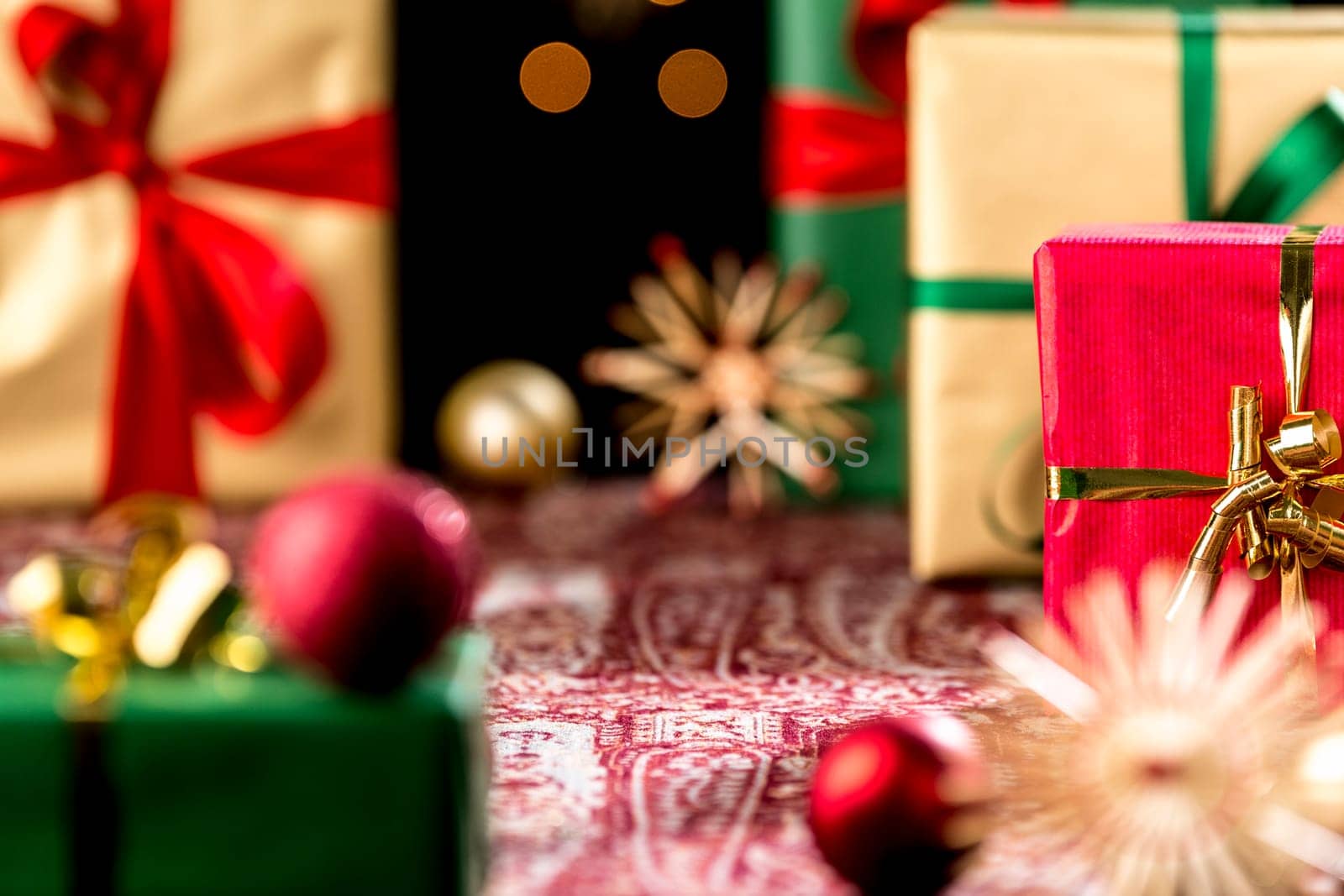 Tightly-framed shot of plain presents in gold and green. Blurred shapes of baubles and stars outside the shallow depth of field. Focus is on the central void and red gift with golden bow.