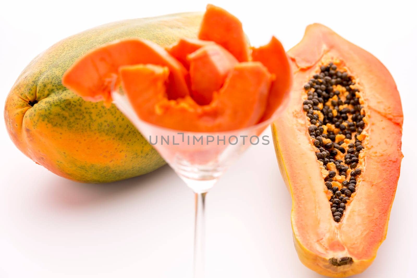 Fruit flesh of the papaya arranged in a glass,but the focus rests on the halved papaya and entire fruit in the back..