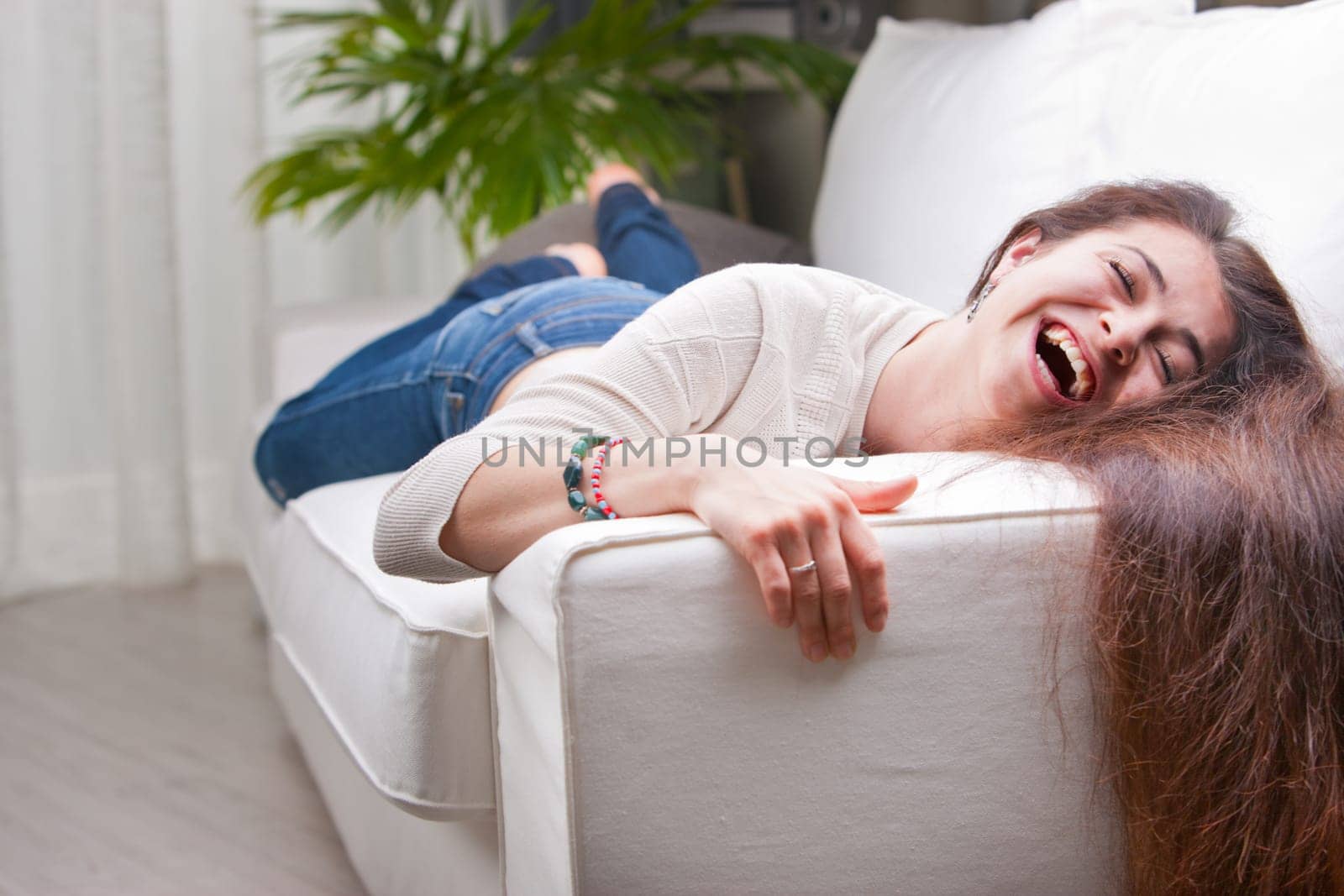 LOL how much could this girl laugh before she could breathe we don't know but she has rings on her hands and a toothy smile that's lovely and she's on a white couch in her living room and she has long brown hair
