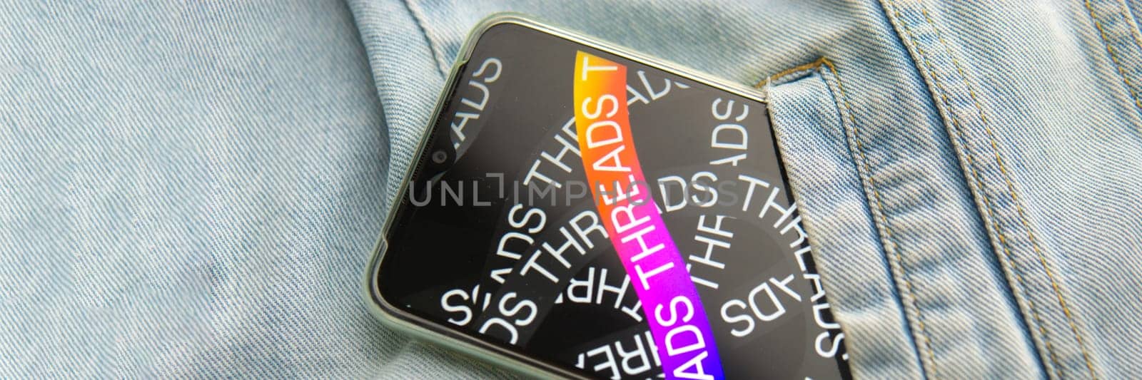 Tver, Russia - July 15, 2023, the threads logo on the smartphone screen lying on the jeans. The threads icon. The logo of the current application. Threads social network