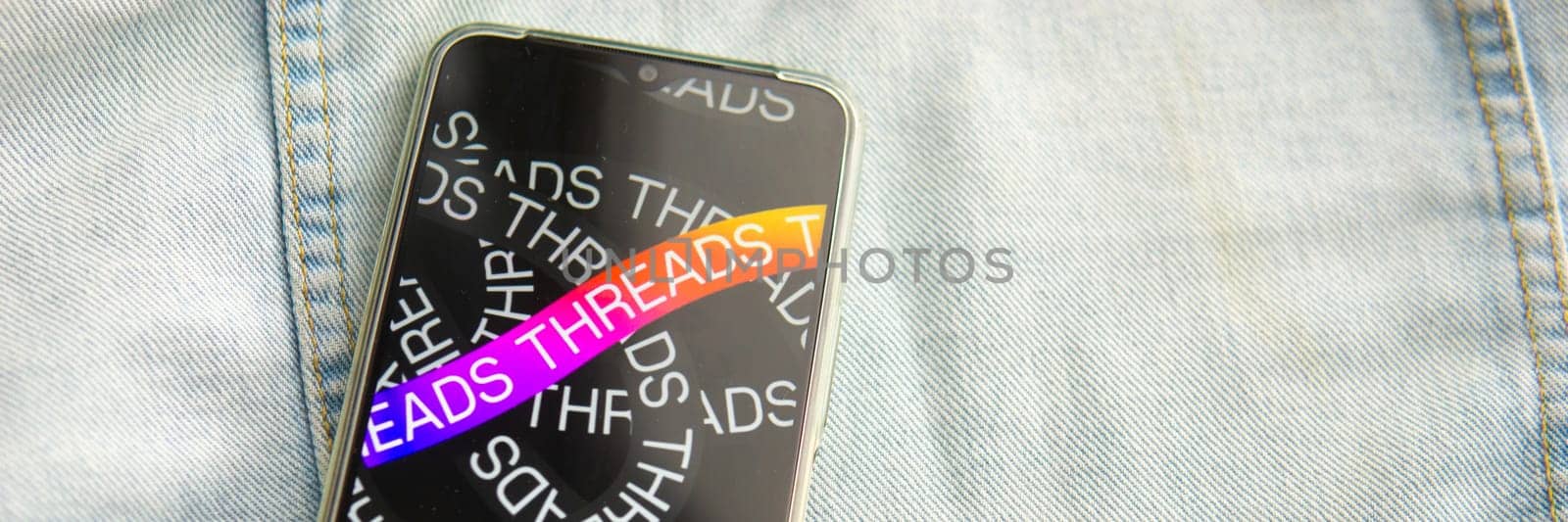 Tver, Russia - July 15, 2023, the threads logo on the smartphone screen lying on the jeans. The threads icon. The logo of the current application. Threads social network. by Annu1tochka