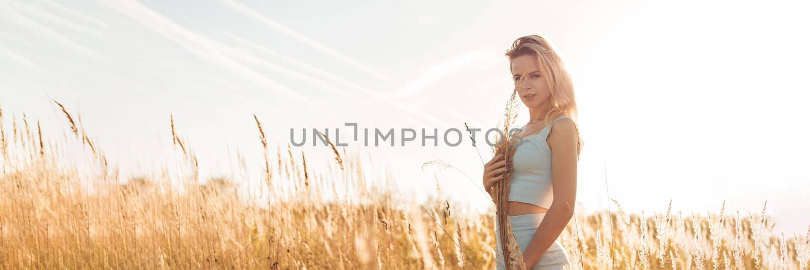 Beautiful blonde woman on a walk in a field with dry grass. A walk in nature, sunset in a field of pampas grass. Life style.