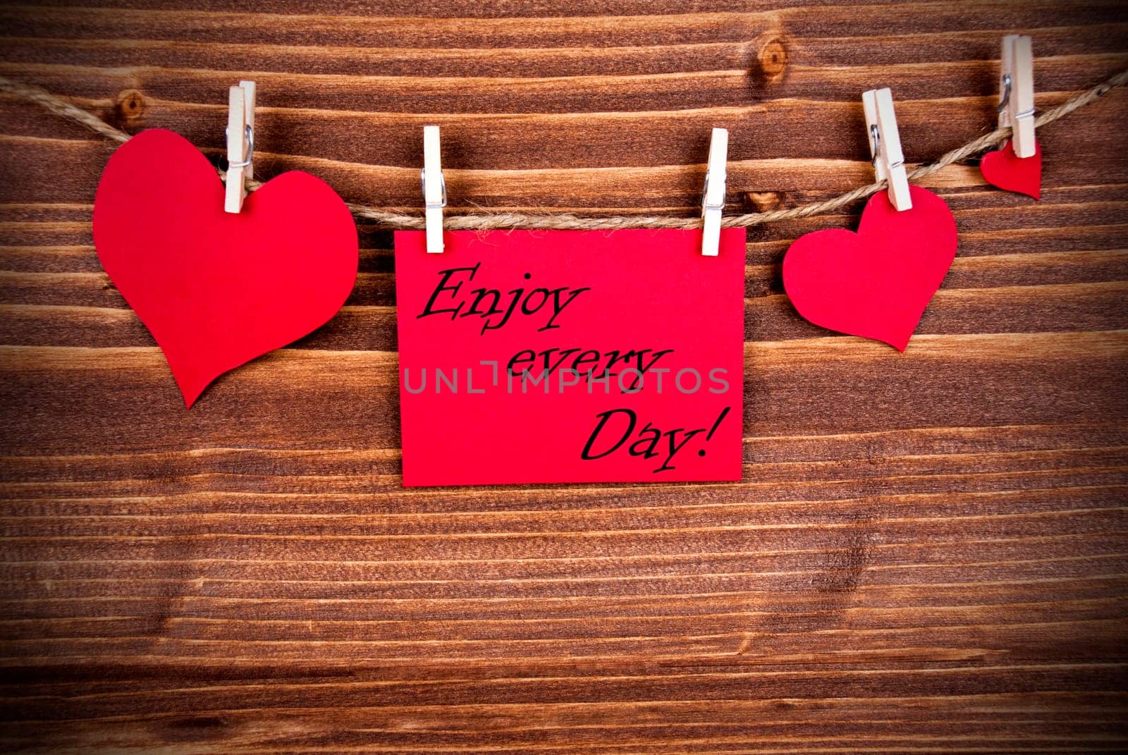 The Saying Enjoy every Day on a red Label with Hearts Hanging on a Line on a Wooden Background