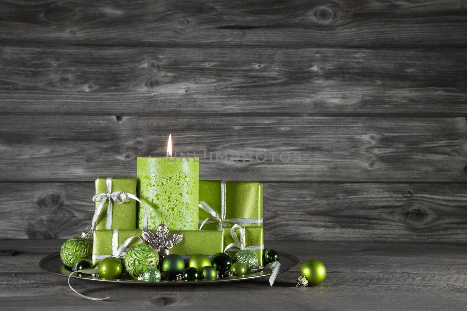 Green christmas decoration with one burning candle and presents on wooden grey background.