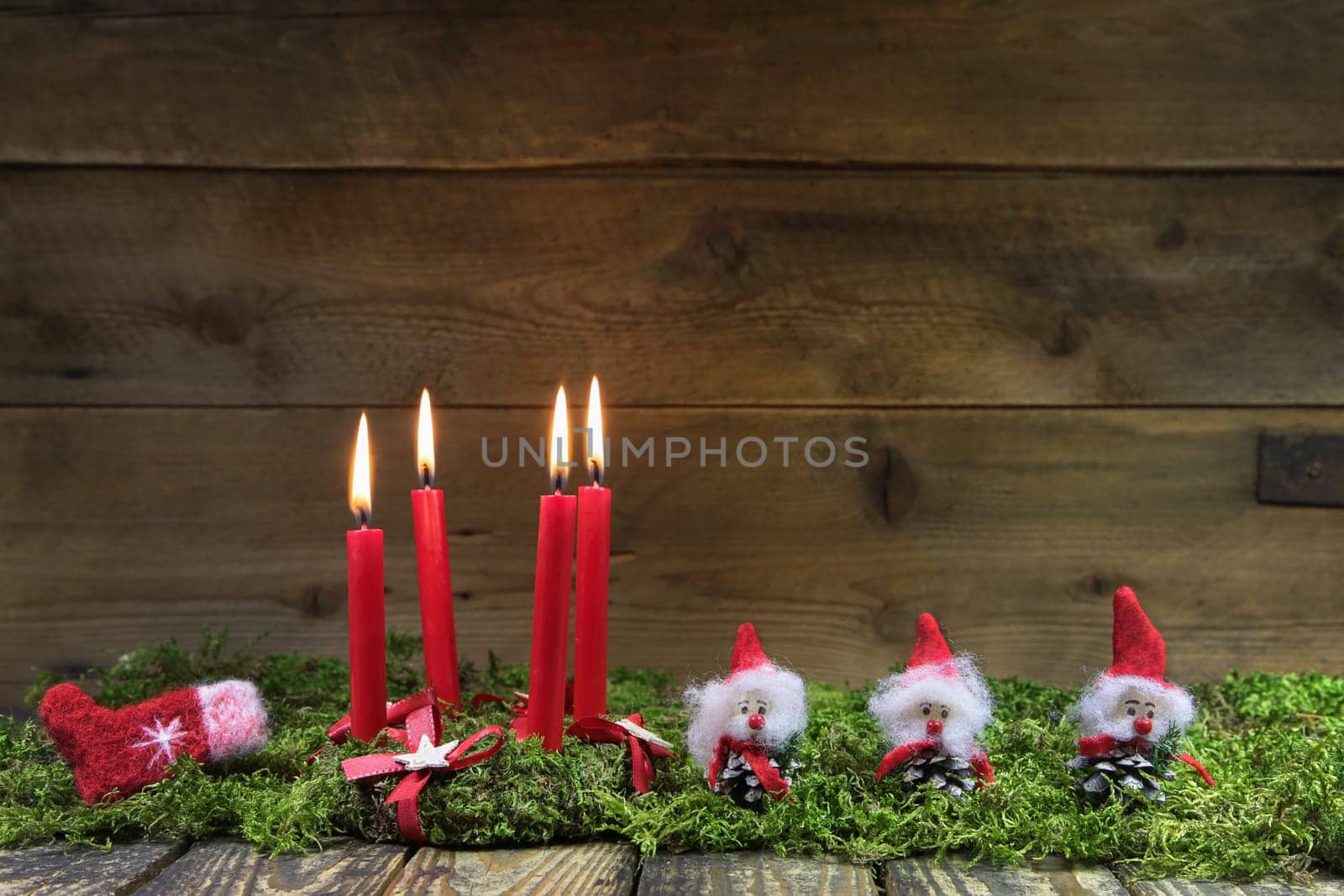 Four red burning christmas candles on wooden background with green moss and brownies.