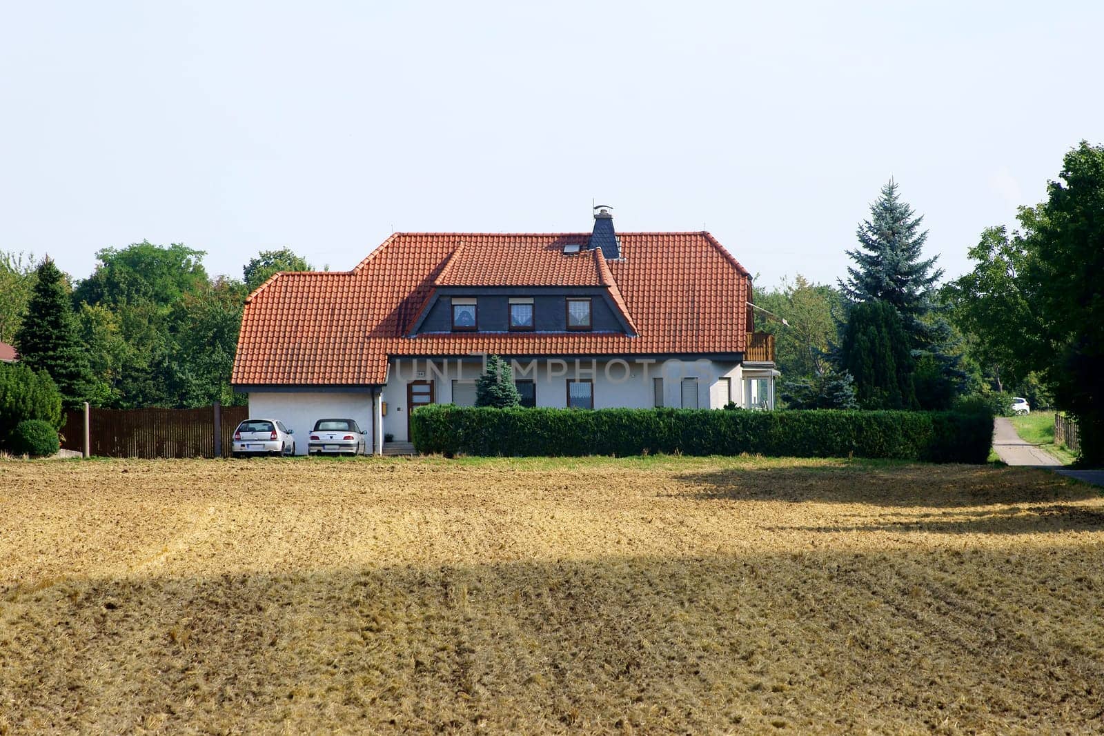 The photograph of a detached house behind a ploughed field.