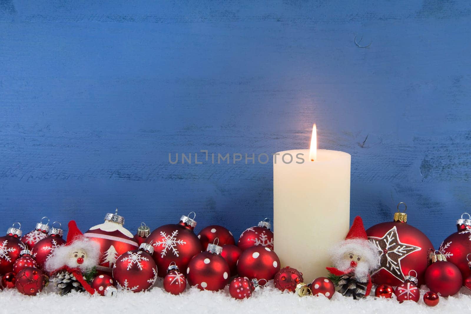 Blue wooden christmas background with a white burning candle and red balls.
