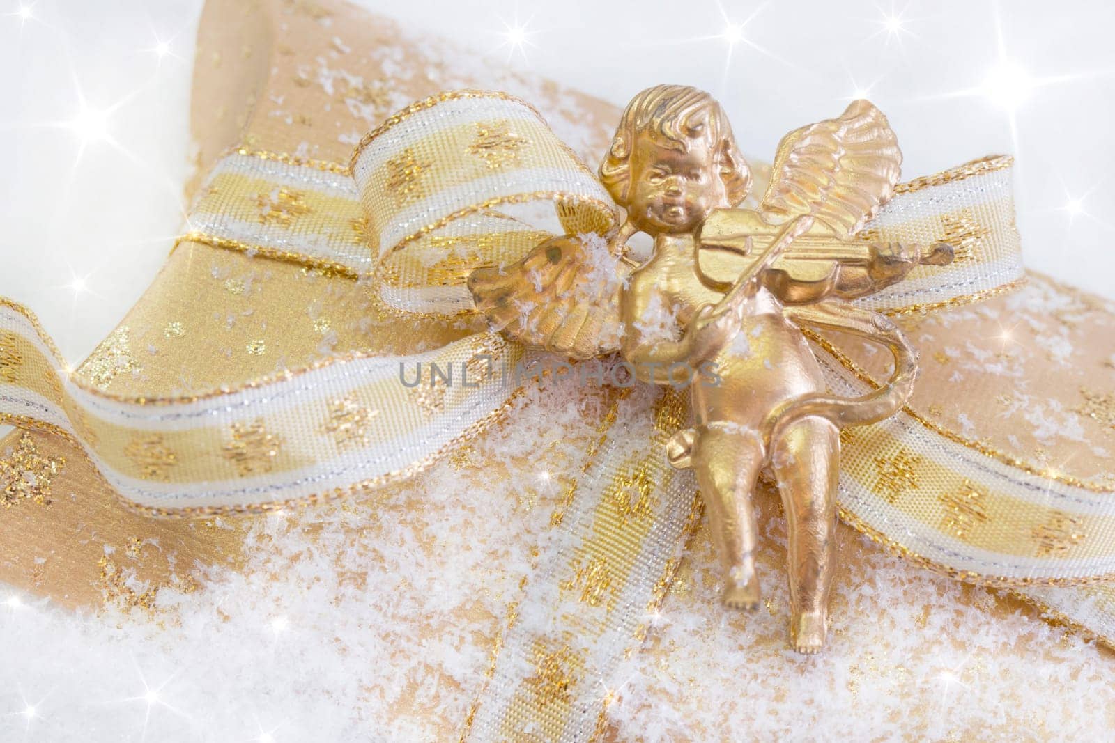 Close up of golden present box with angel playing violin for christmas on snowy background
