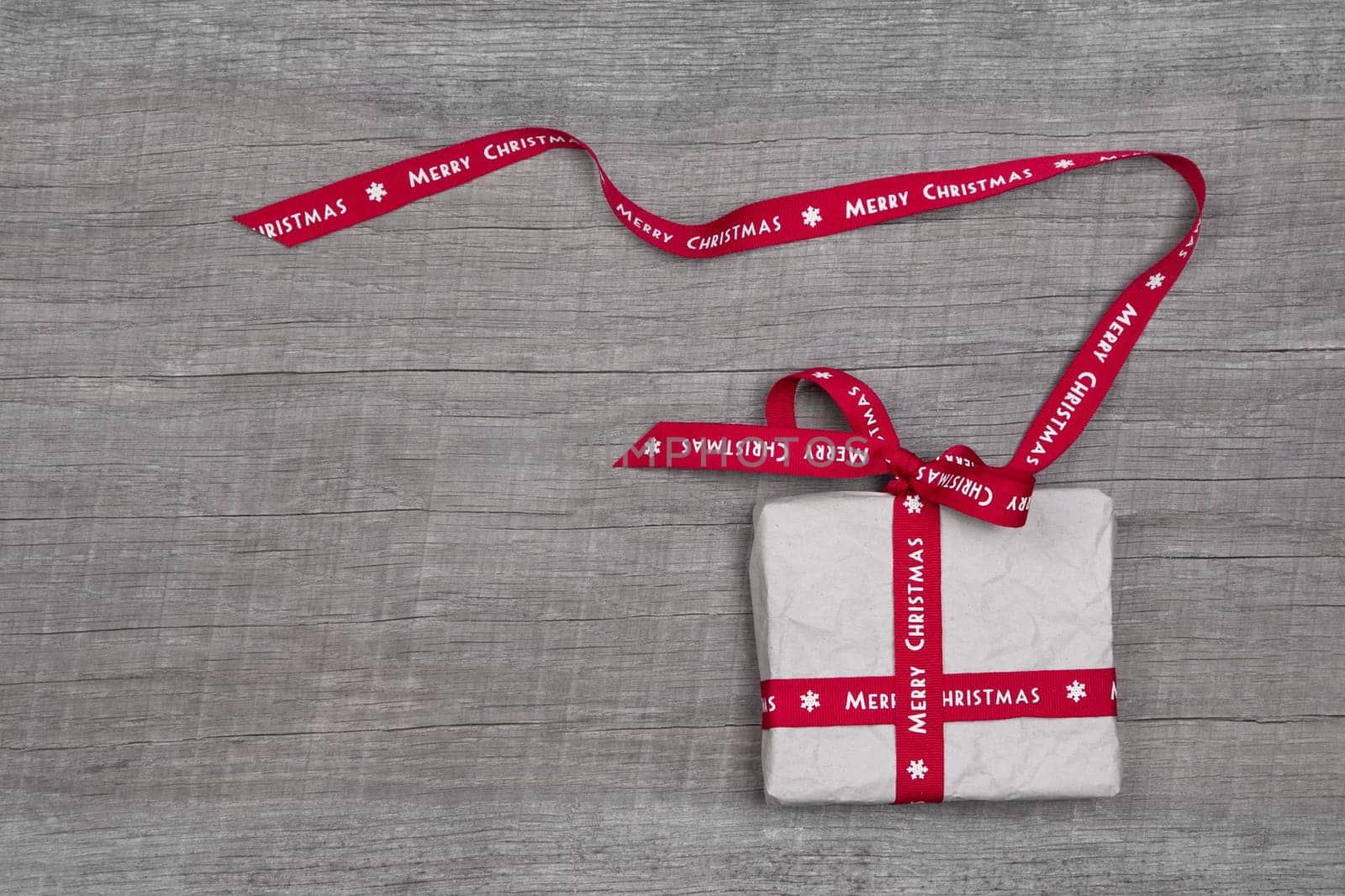 White Christmas gift box with red ribbon on grey wooden background