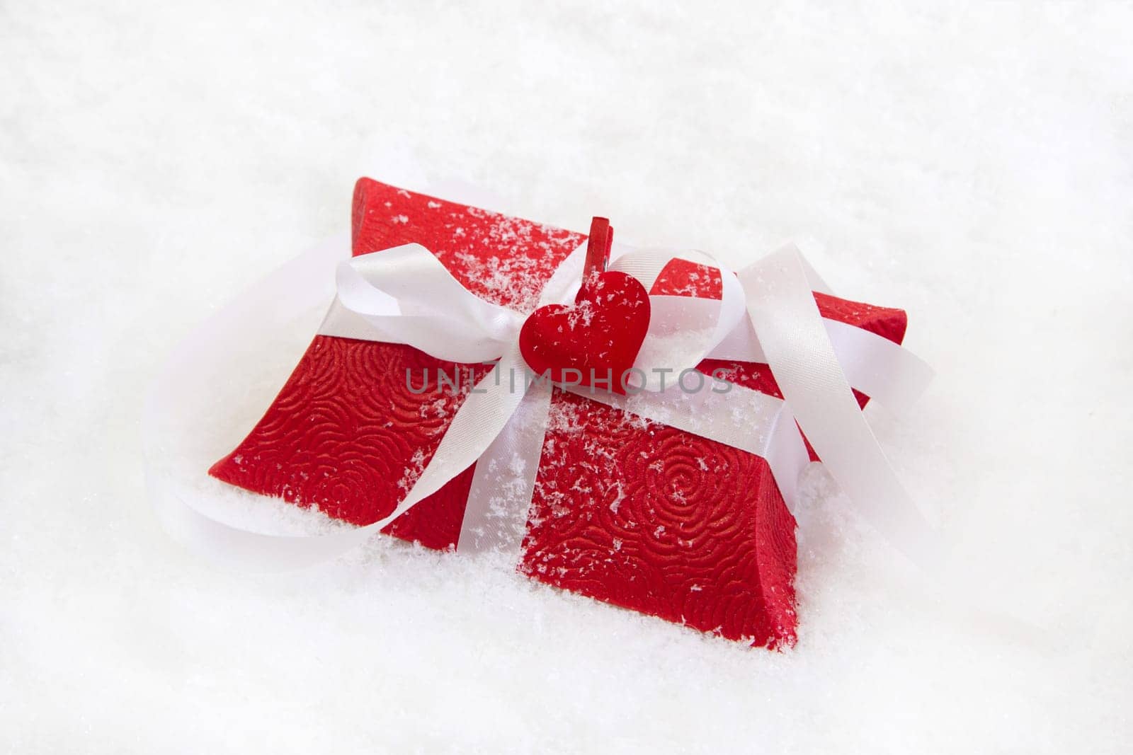 Red present box with white ribbon for christmas on white background with snow and a red heart