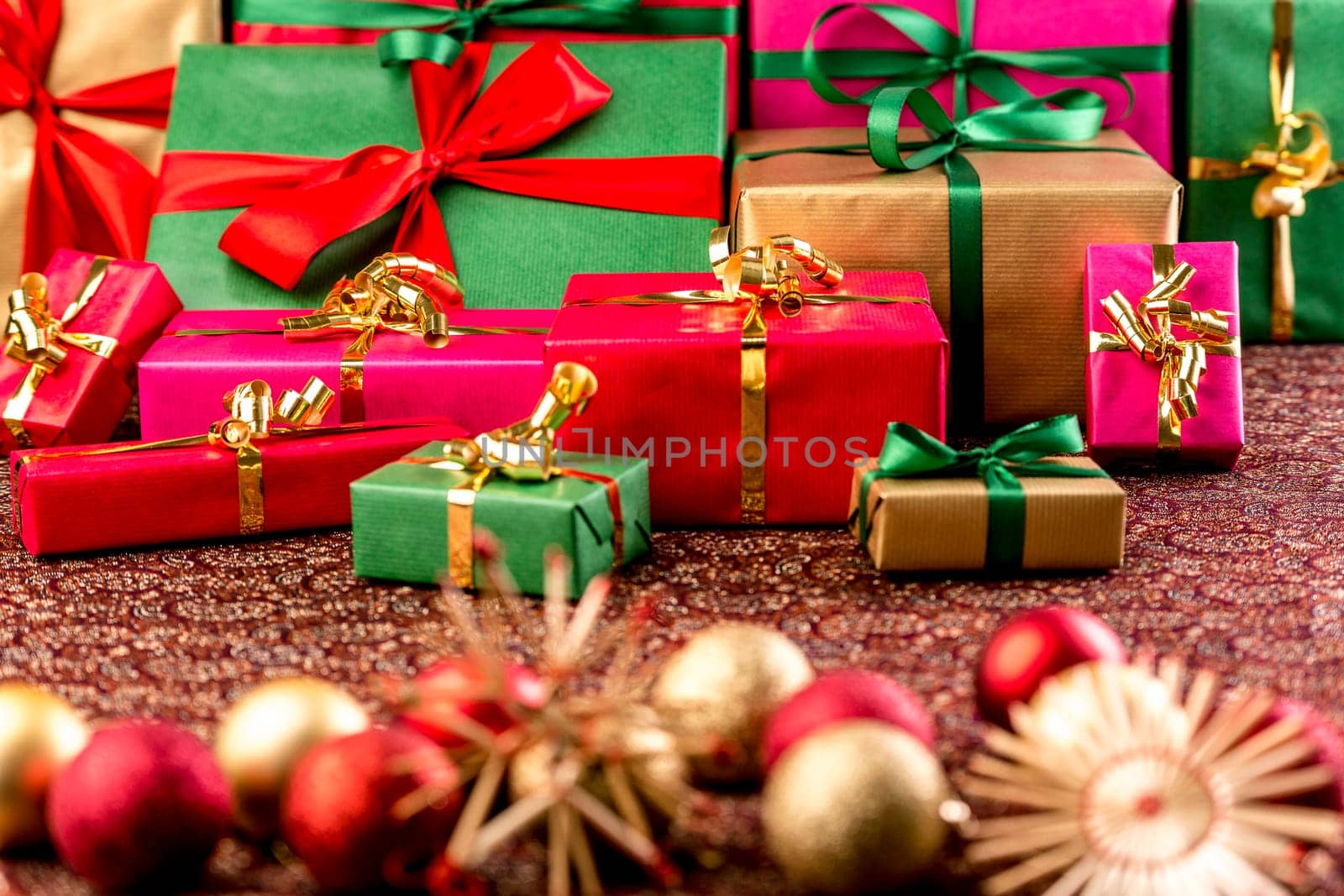 Christmas gifts piled up for handing out of presents. Wrapped in green red,gold and magenta. Straw stars and Xmas ornaments outside the shallow depth of field..