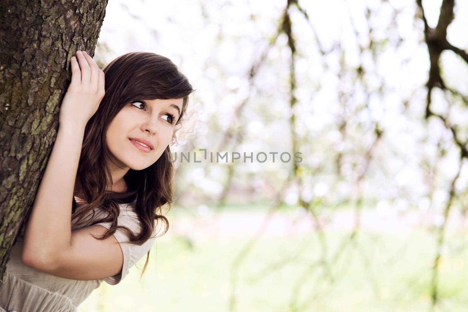 Beautiful young woman hiding behind tree trunk