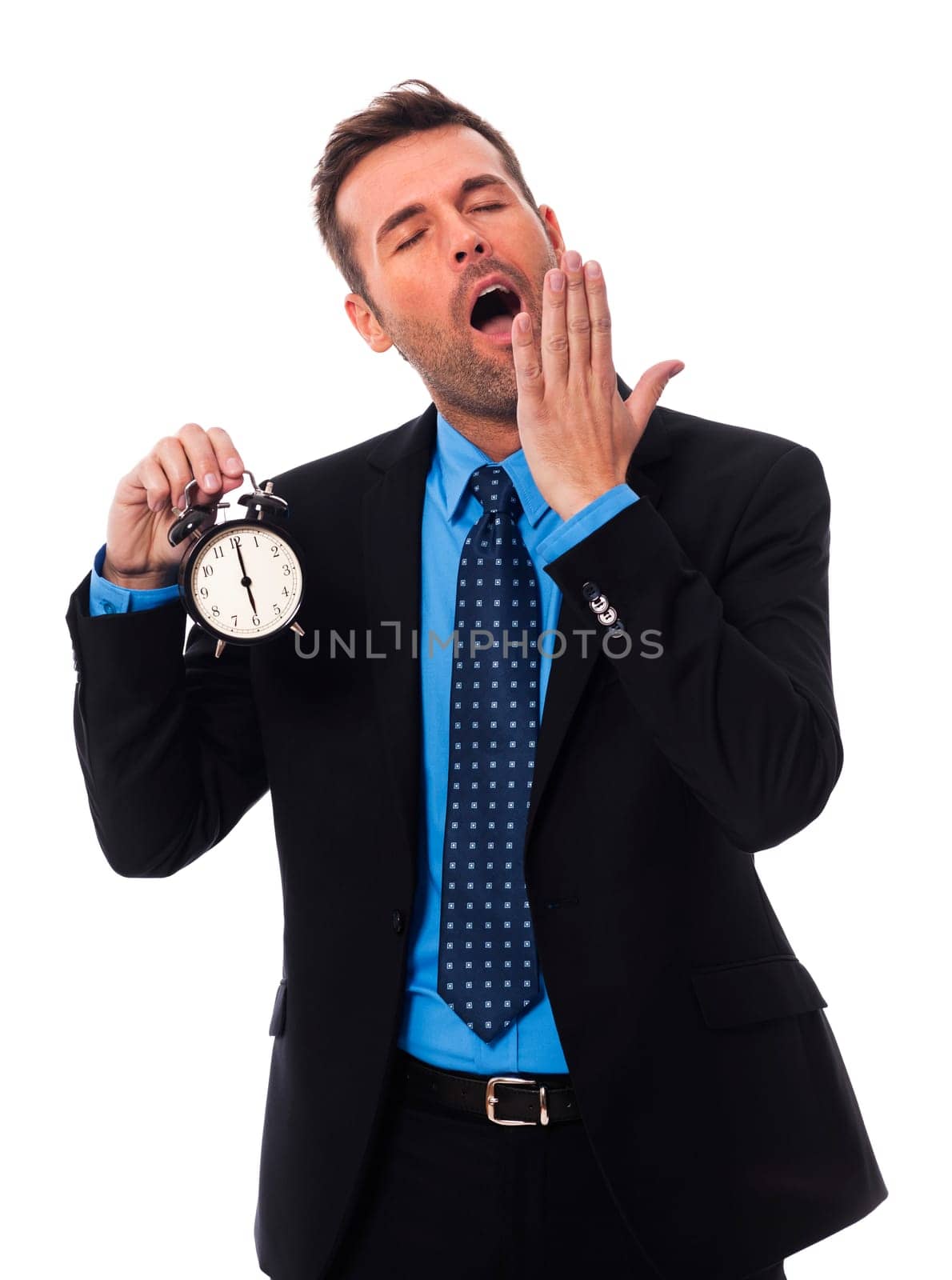 Yawning businessman holding alarm clock