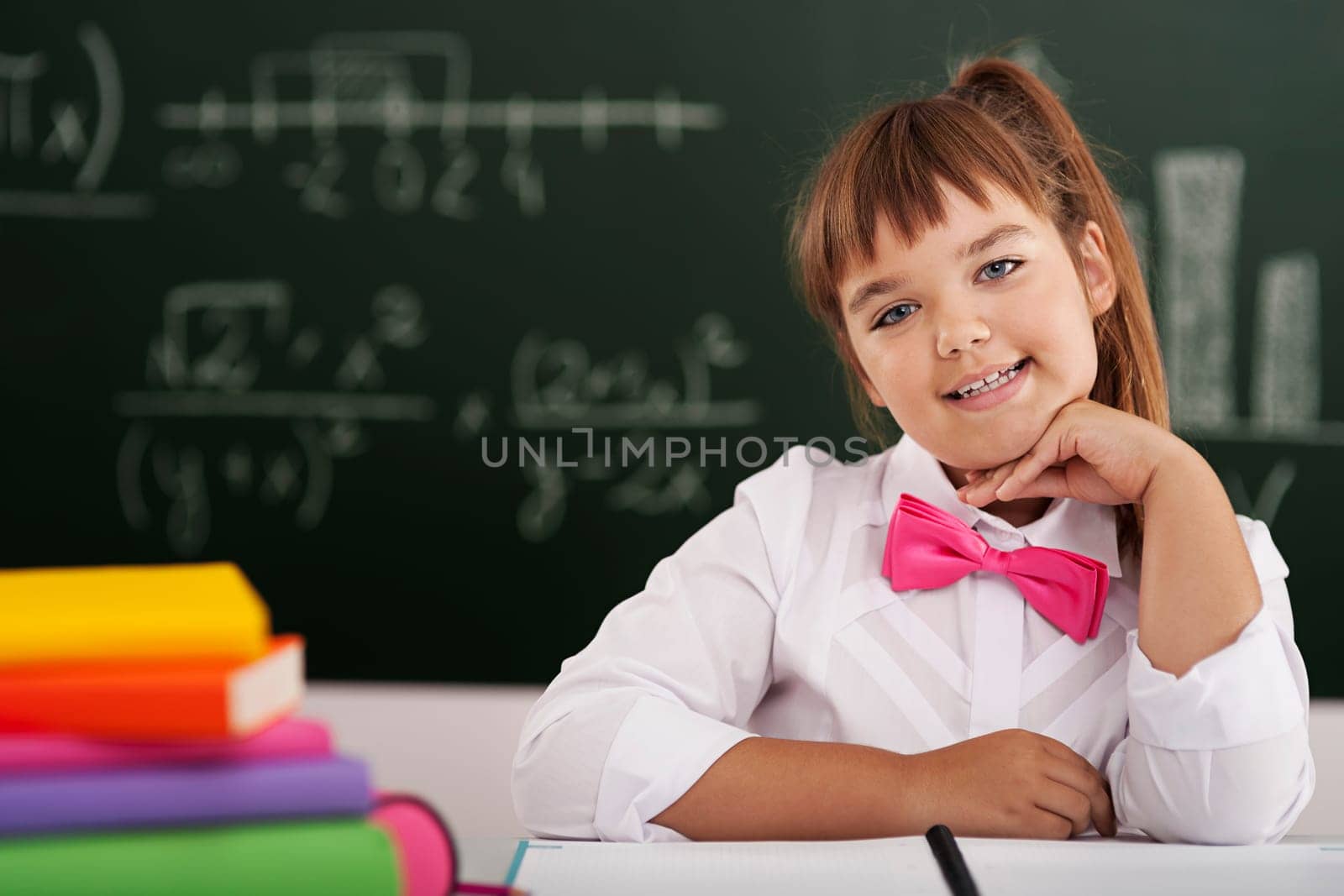 Cute little schoolgirl sitting in classroom with her books