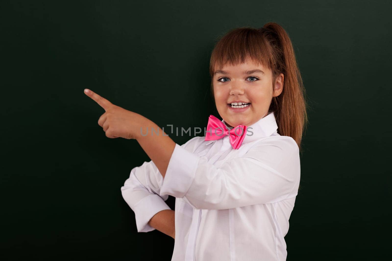 Smiling girl with pink bow tie pointing at copy space
