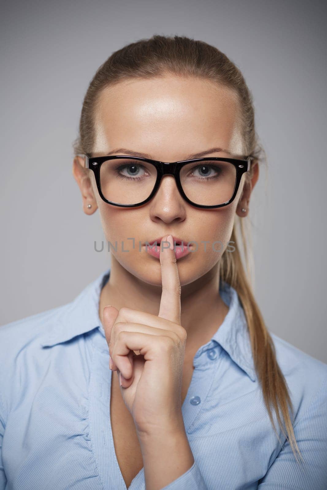 Serious woman wearing glasses showing quiet hand sign