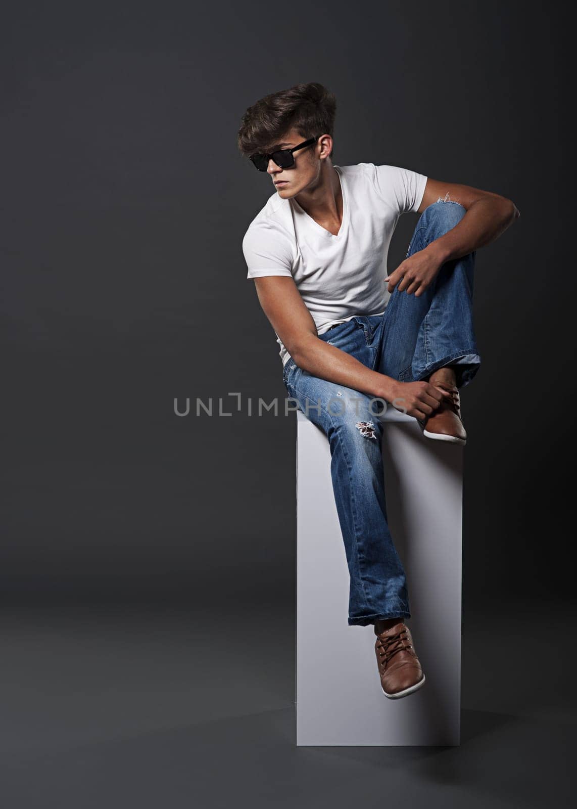 Young fashion man sitting on white rectangle