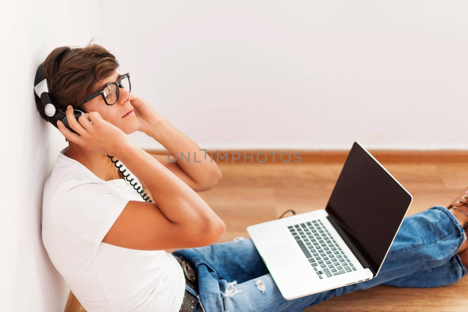 Handsome hipster sitting up against wall listening to music