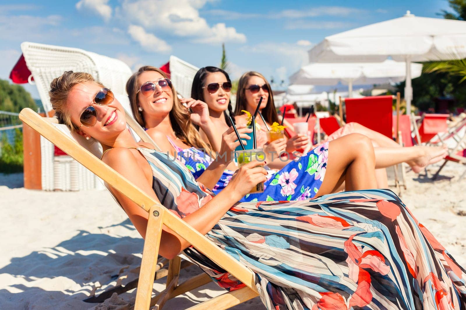 Four women drink cocktails in a beach club and lie on a sun lounger