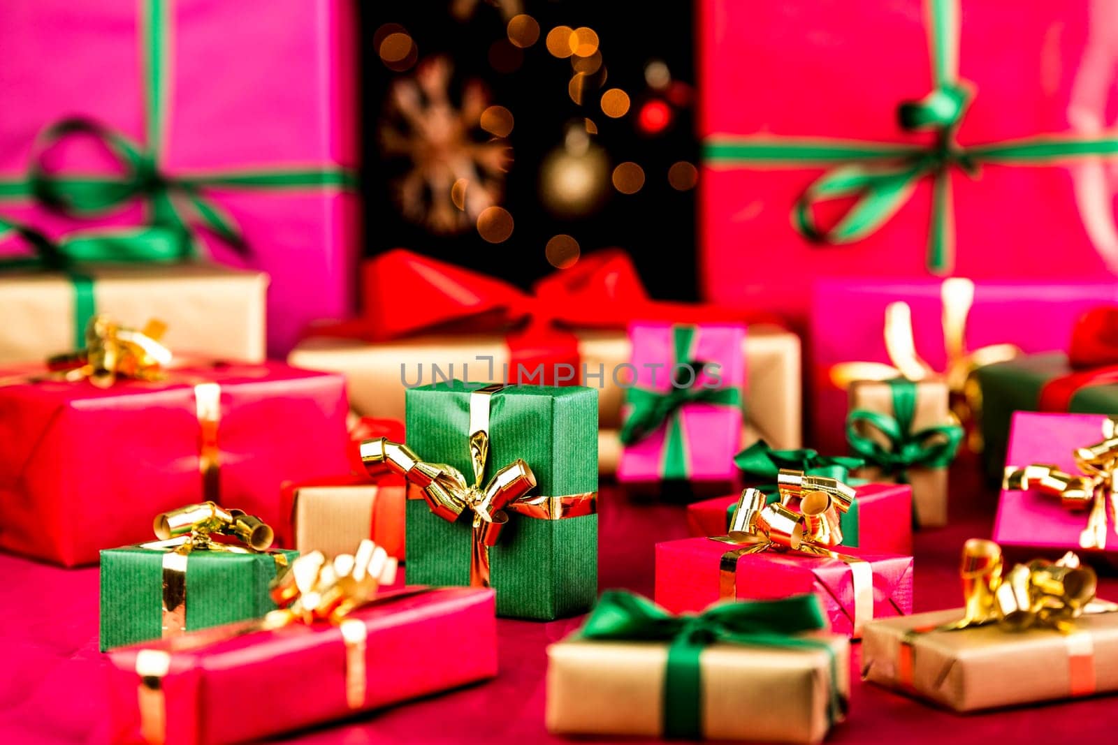 Plenty of single-colored Christmas presents placed on a red, smooth cloth. Vibrant colors. Narrow depth of field. Blurred baubles and stars over pitch black background. Most gifts in soft focus..