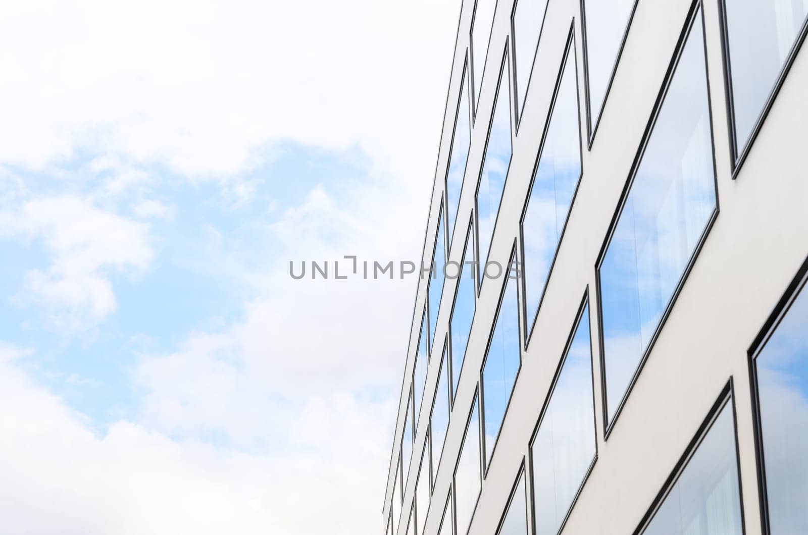 Blue sky and clouds reflected in mirrored windows of new modern building glass facade. Background with free copy-space area for your text.