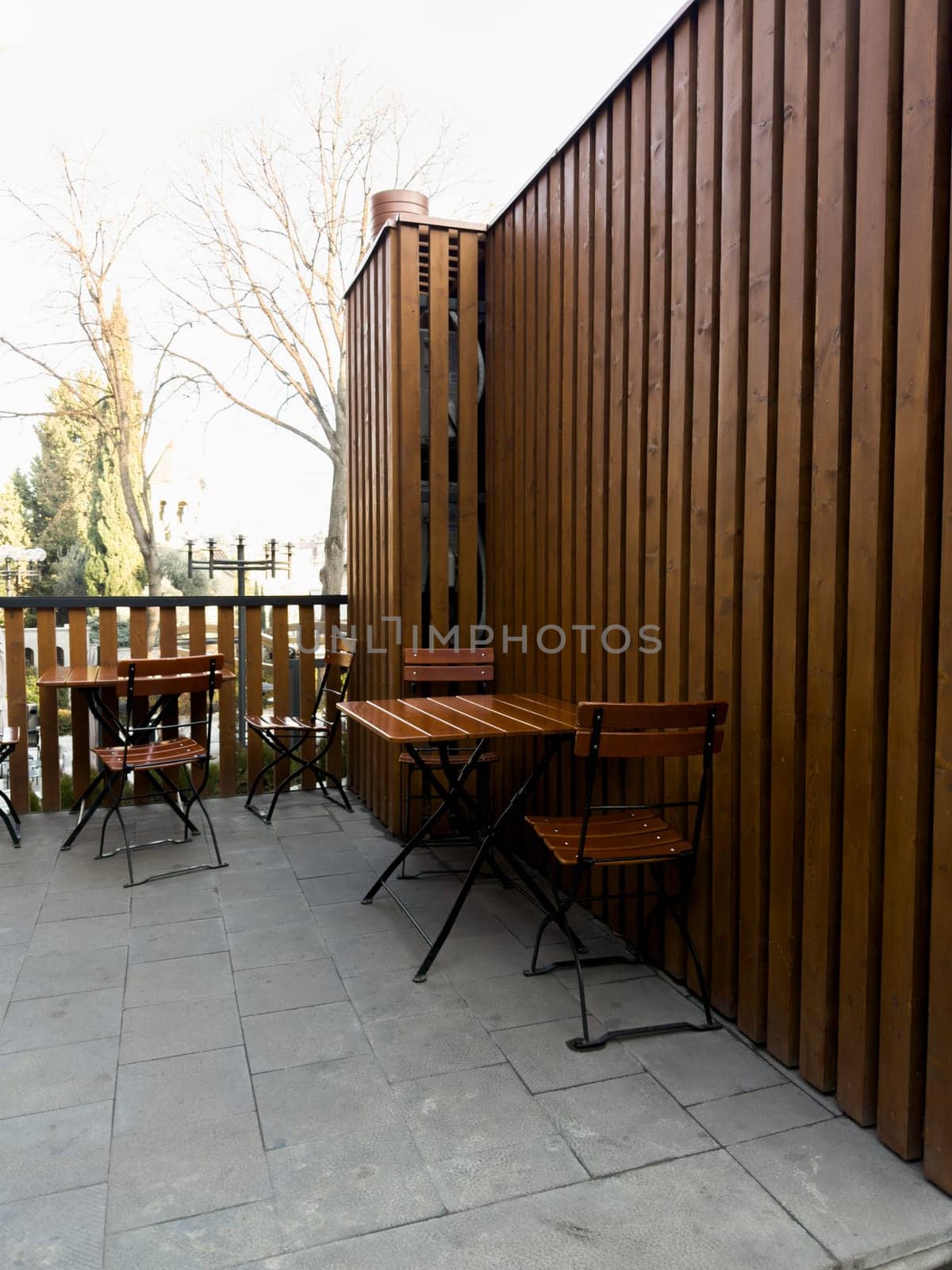 Vertical photograph of summer cafe with wooden chairs and tables. Nice outdoor cafe made of wood. Eating on terrace in good weather. Simple cafe on street to relax while walking around city