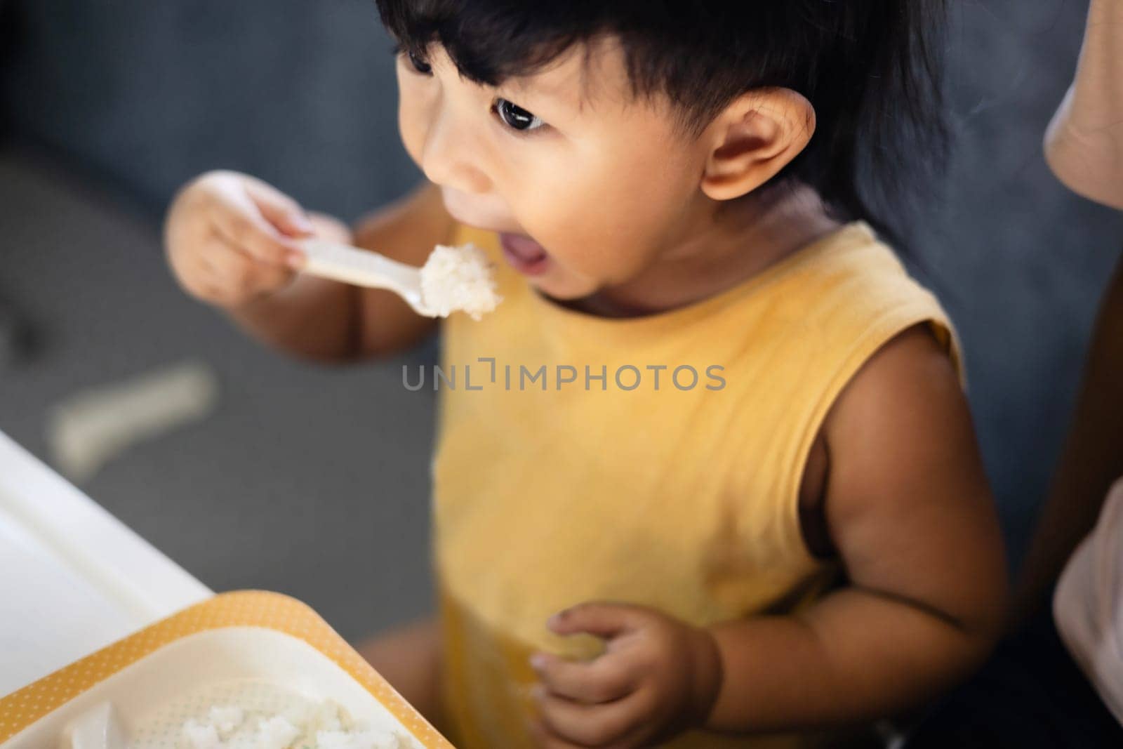 The little boy eating rice with a spoon. Happy child eats rice with a spoon in his hand.