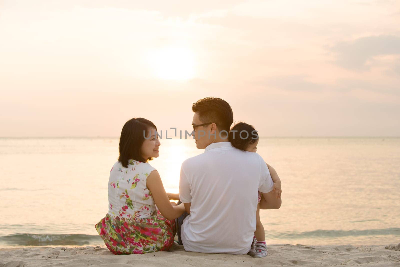 Portrait of young Asian family seated on beach outdoor vacation, during summer sunset, natural sunlight.