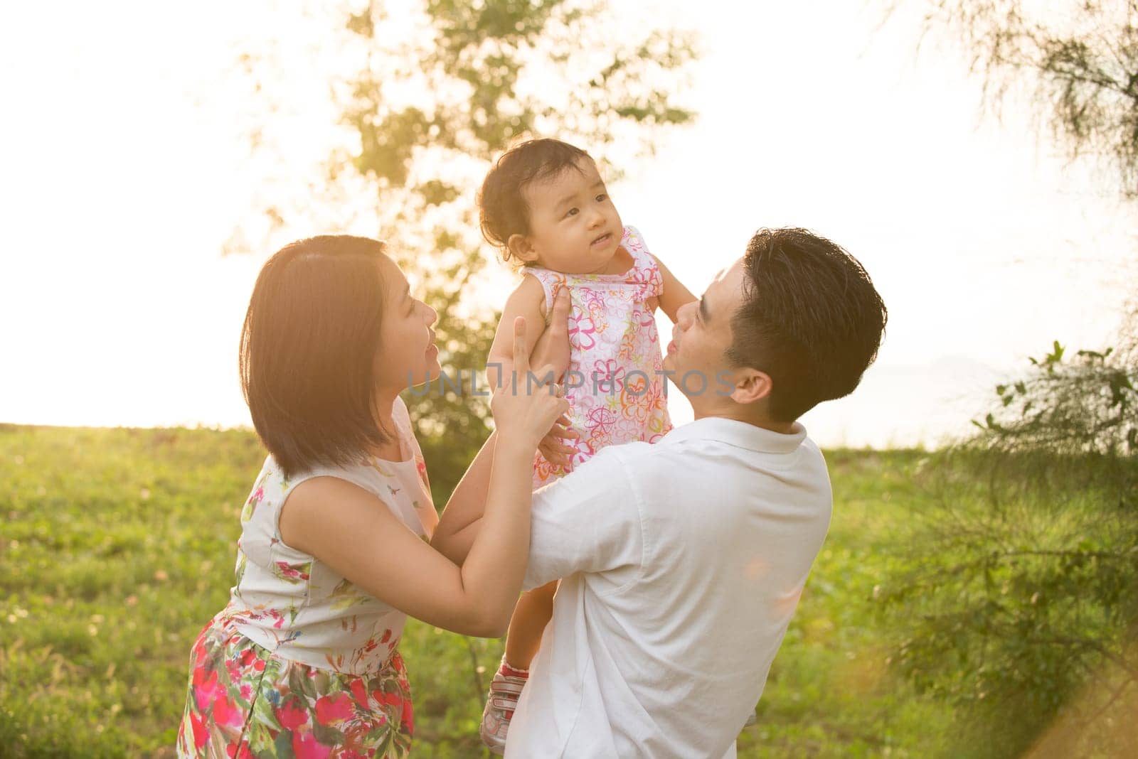 Portrait of joyful happy Asian family playing together at outdoor park during summer sunset.