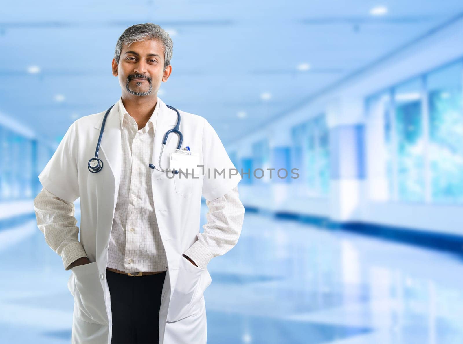 Indian doctor. Mature Indian male medical doctor standing inside hospital. Handsome Indian model portrait.