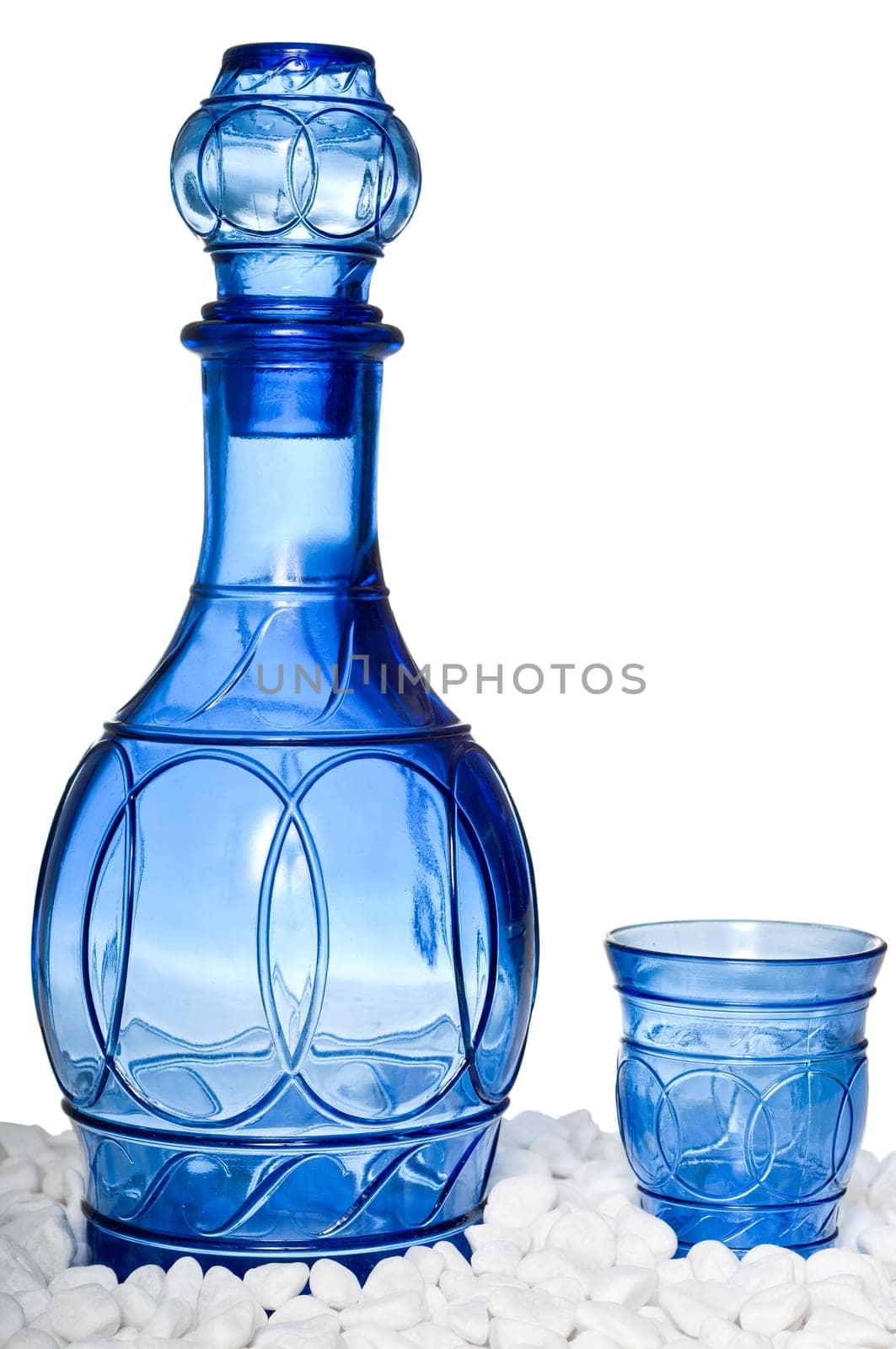 Blue bottle and tumbler on white stones, isolated on a white background
