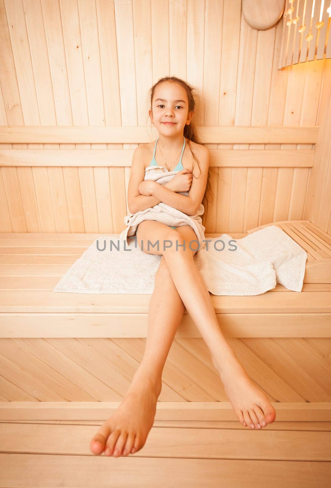 Photo of young girl with long legs sitting on towel at sauna