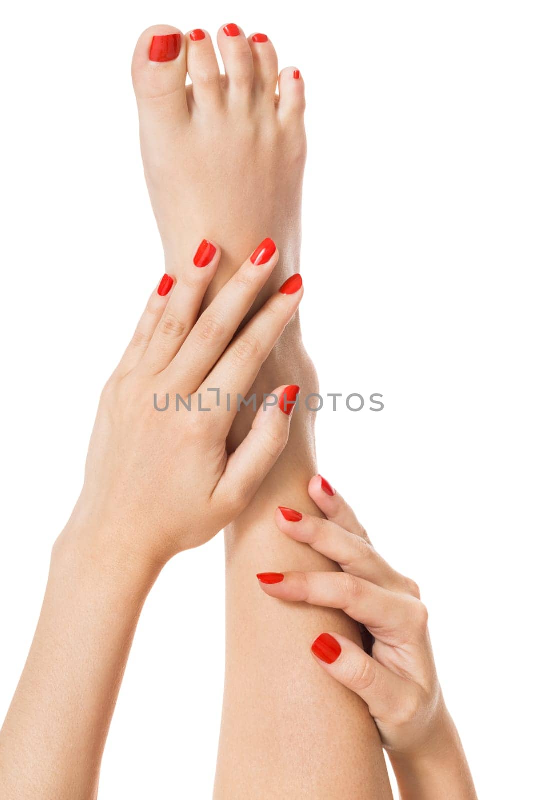 Woman with beautiful neatly groomed red finger and toe nails sits with bare feet clutching her ankles with her hands on white in a concept