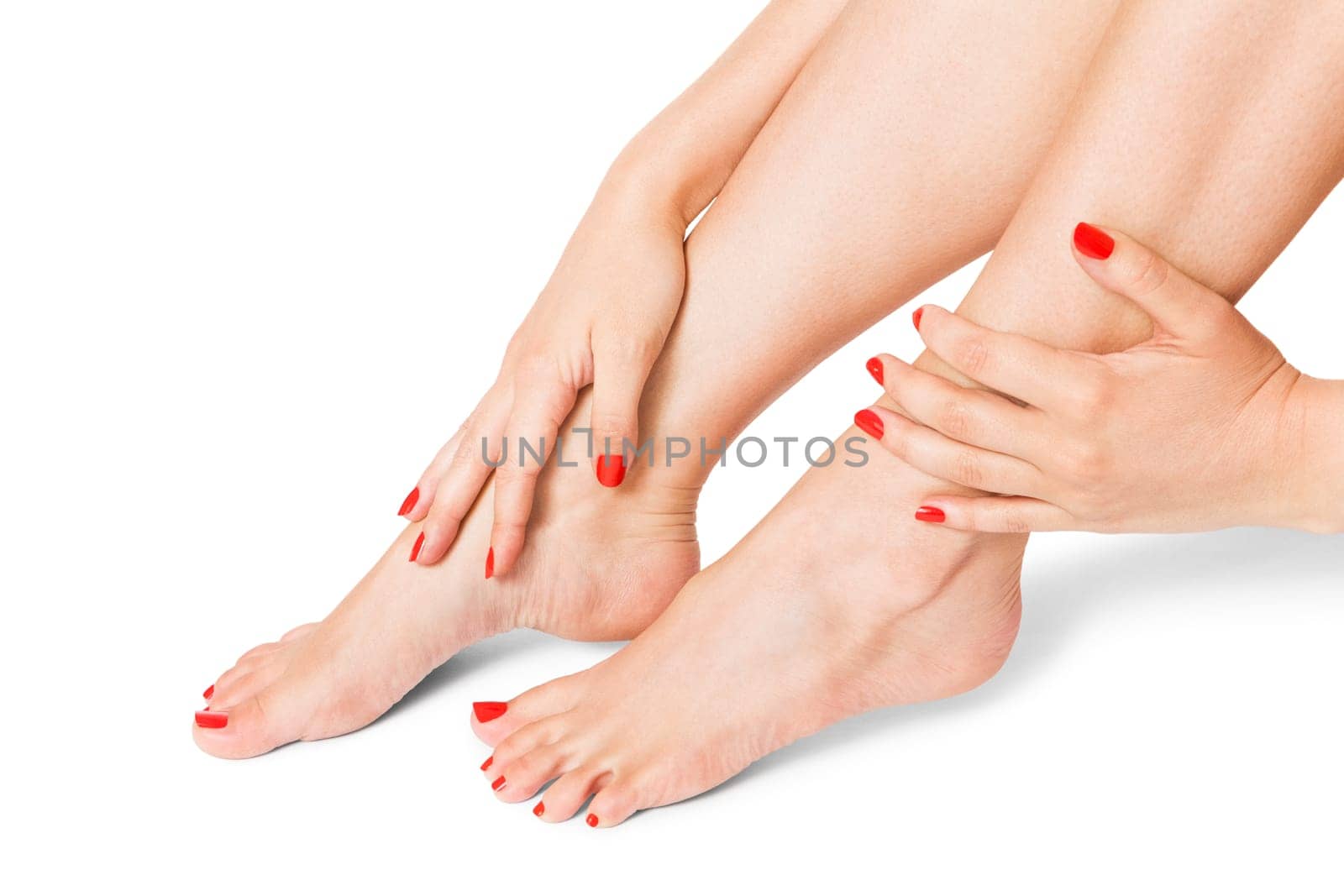 Woman with beautiful neatly groomed red finger and toe nails sits with bare feet clutching her ankles with her hands on white in a concept