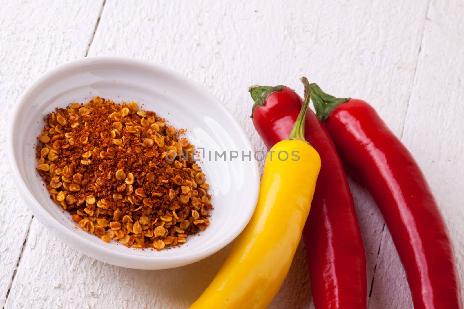 Fresh pepperoni and chilli with chili powder as a close-up on a white rustic wooden board