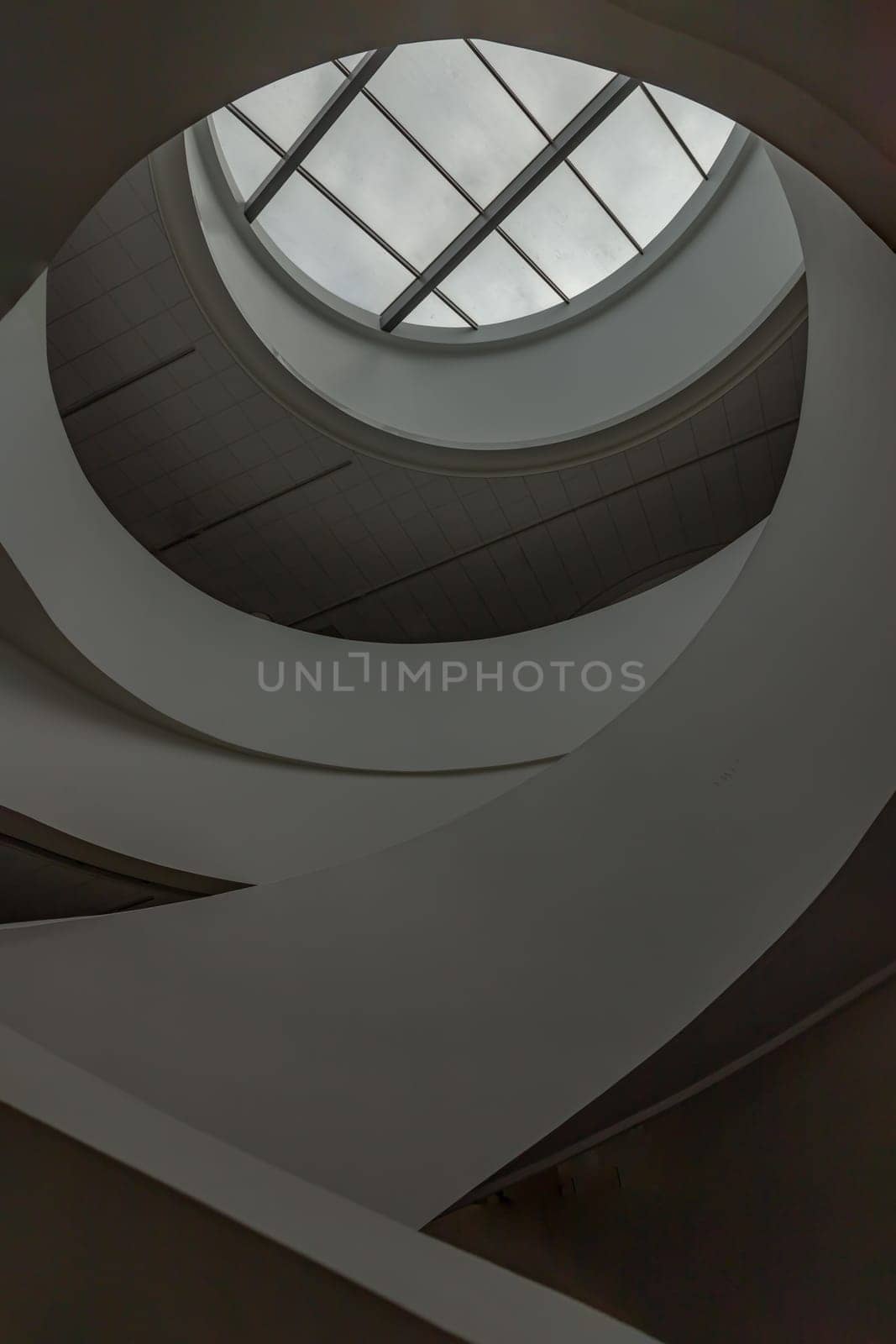 Looking up to the sky through modern channel round circular ceiling with spiral staircase. The white ceiling with Huge transparent circular glass panel on the middle as a main skylight showing sky above, Glass ceiling, Space for text, Selective Focus.