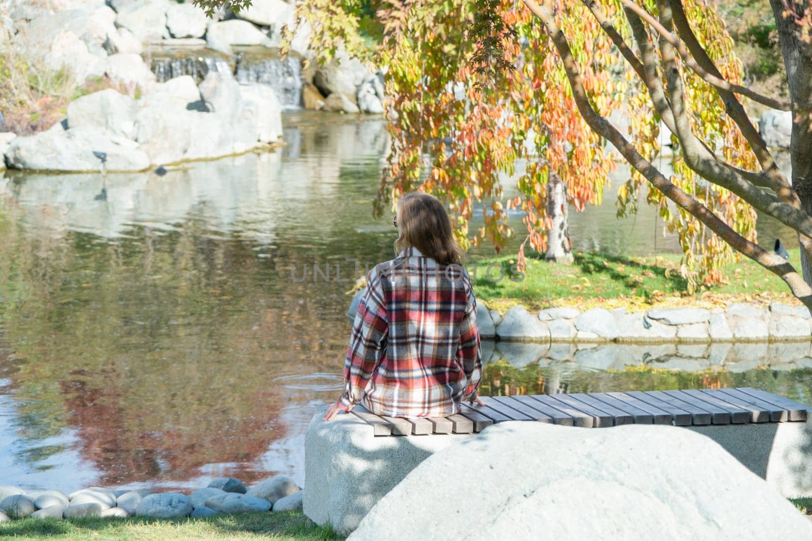 Woman in red plaid shirt enjoying nature sitting in Japanese Garden