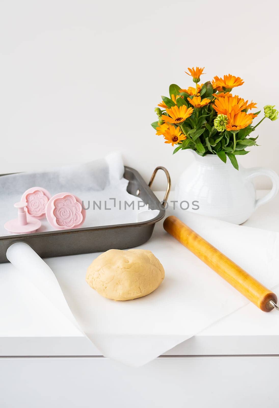 Preparation of the dough for making cookies with molds in the form of flowers, a rolling pin, a bouquet of orange flowers and a baking tray. Concept of family and cooking