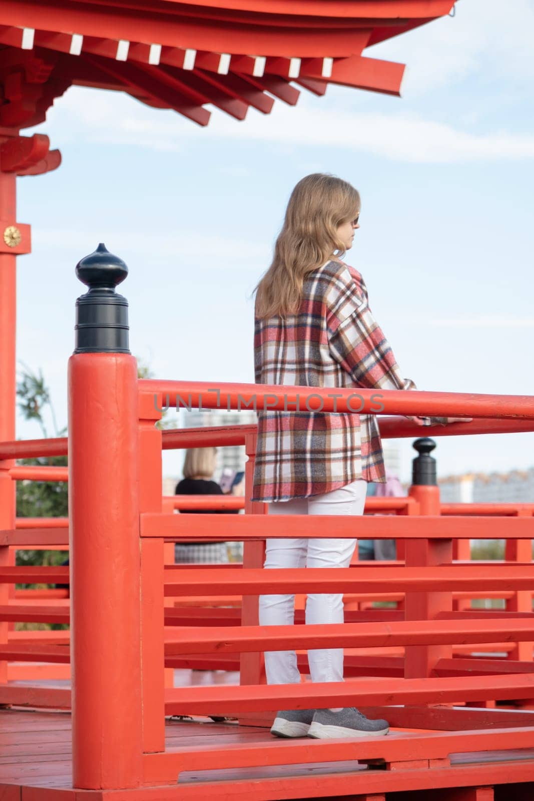 back view of unrecognizable Woman in red plaid shirt enjoying nature walking in Japanese Garden with red pagoda