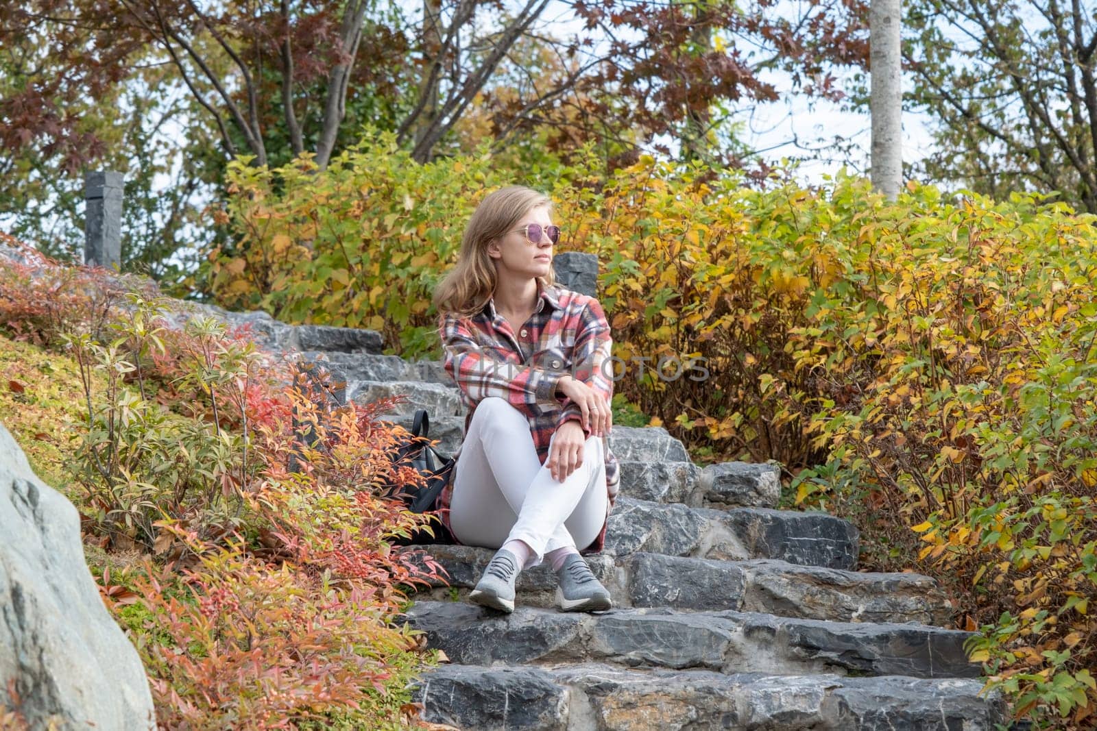 Woman in red plaid shirt enjoying nature sitting in Japanese Garden