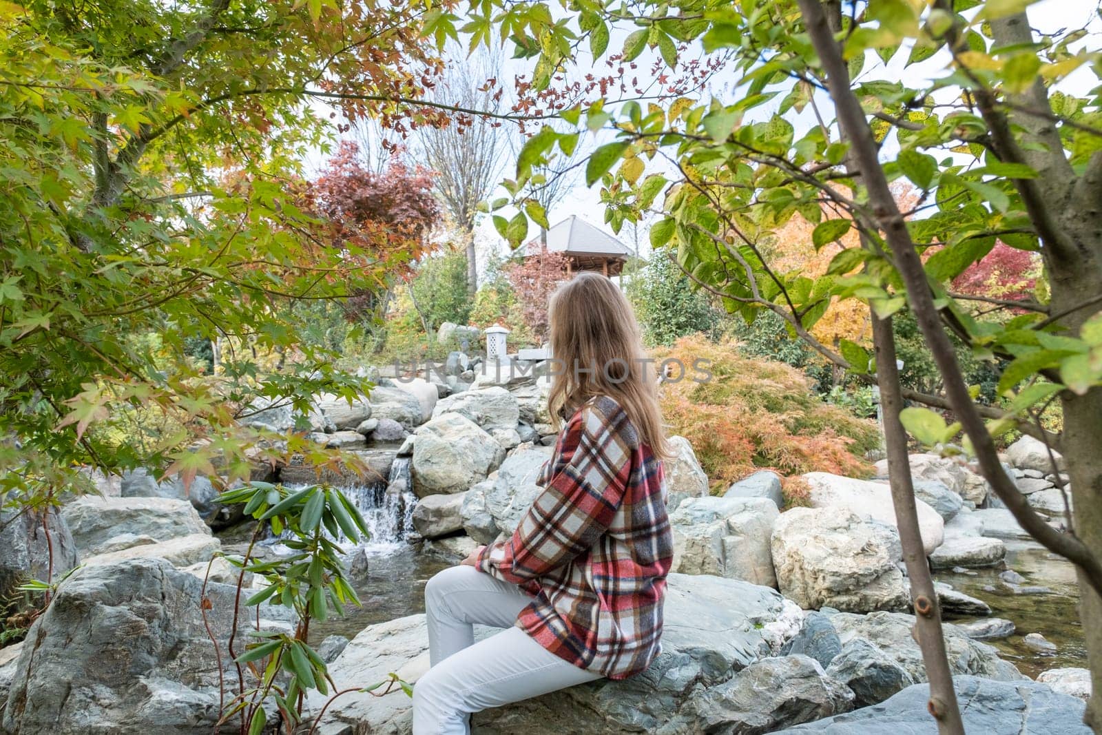 Woman in red plaid shirt enjoying nature sitting in Japanese Garden