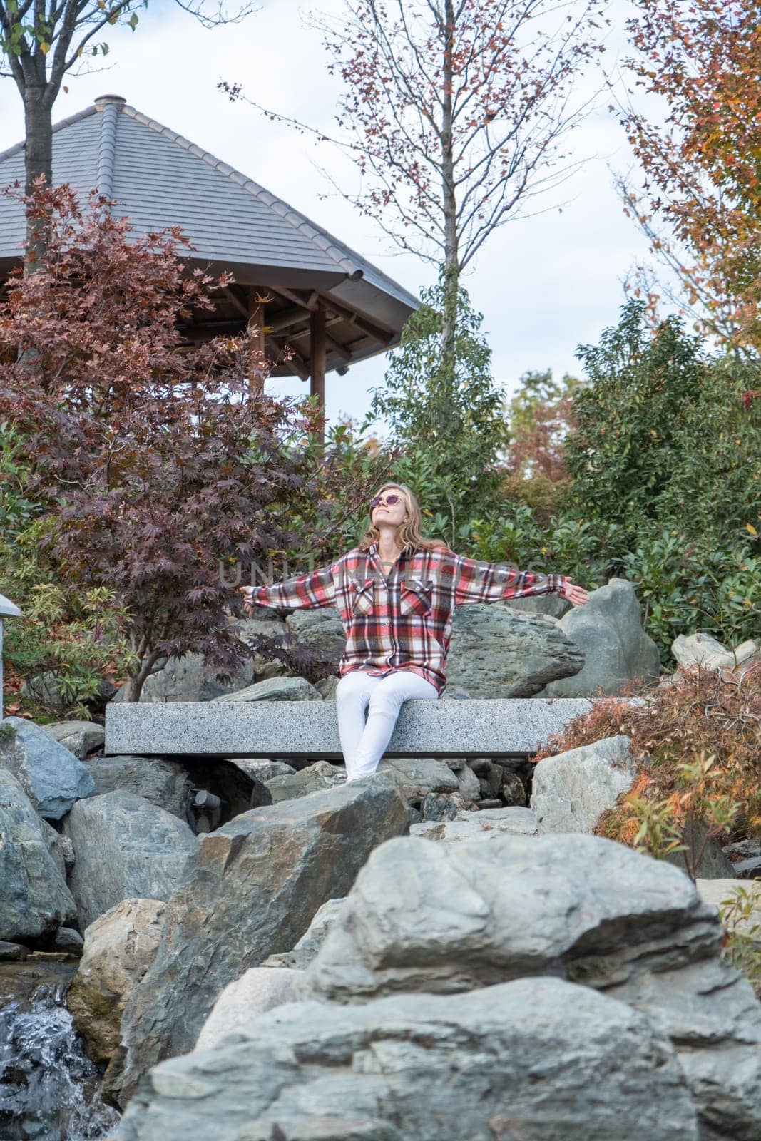 Woman in red plaid shirt enjoying nature sitting in Japanese Garden