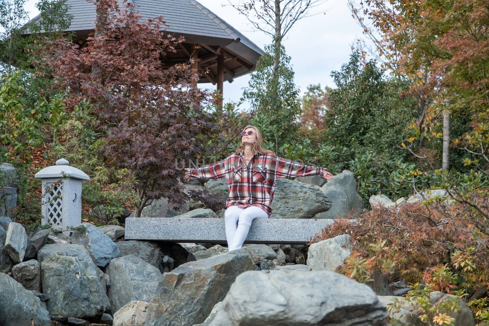 Woman in red plaid shirt enjoying nature sitting in Japanese Garden