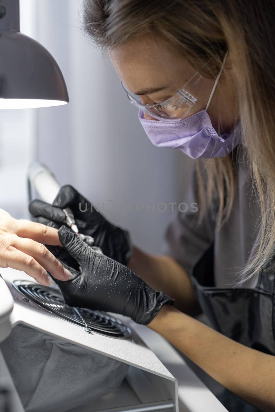 Manicurist at work. Professional manicurist removes old worn nail design from nails of client using modern electric drill. Preparing fingernails for making fresh manicure and applying new nail design