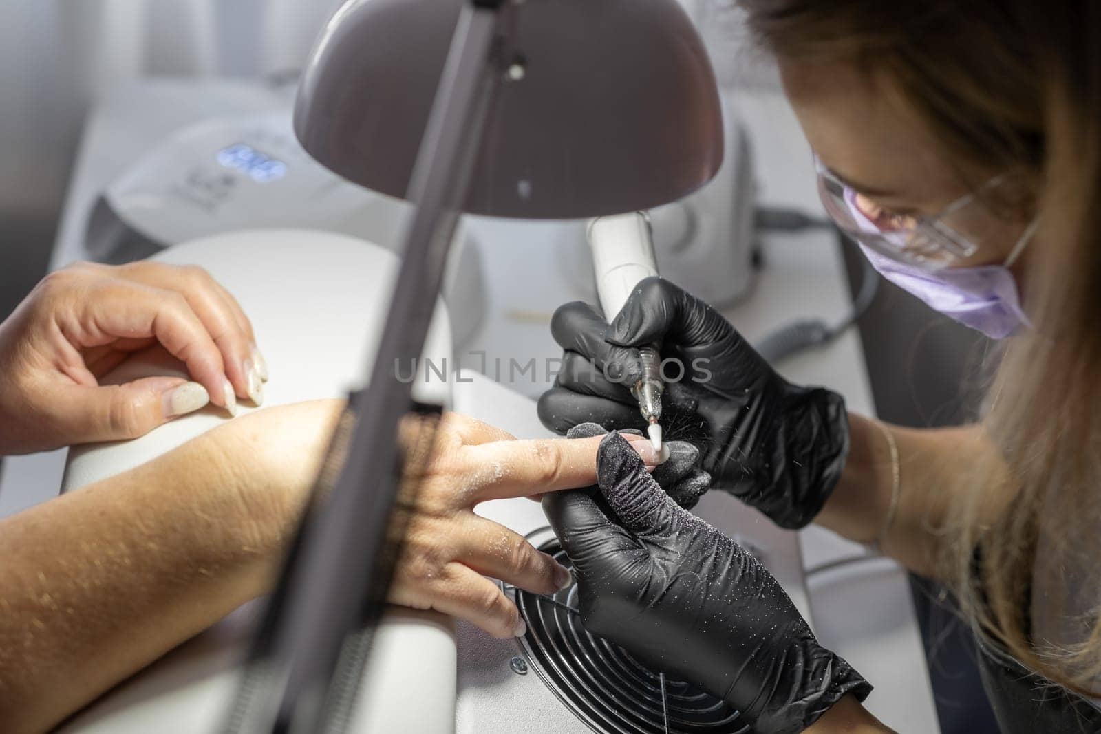 Manicurist at work. Professional manicurist removes worn nail design by AnatoliiFoto